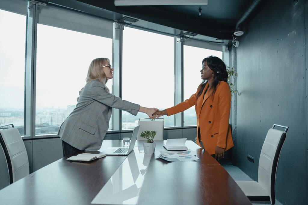 Two businesswomen shaking hands in a modern office setting, symbolizing partnership and agreement.